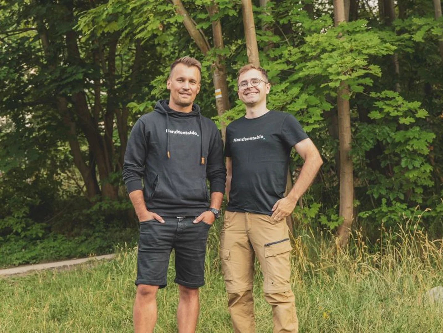 Handsontable's co-founders, Chris Spilka and Marcin Warpechowski, standing side by side in Handsontable T-shirt and hoodie in front of trees.