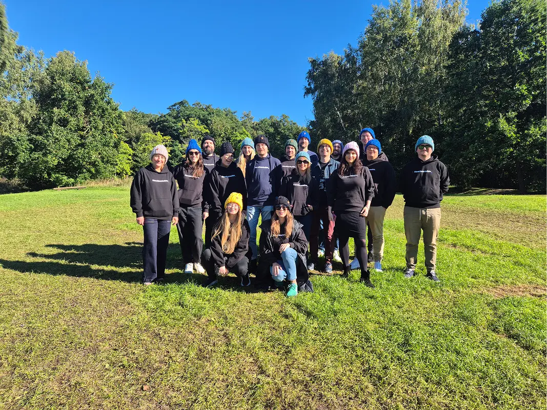 The Handsontable team in matching dark hoodies and beanies, standing together on a sunny lawn in front of trees.